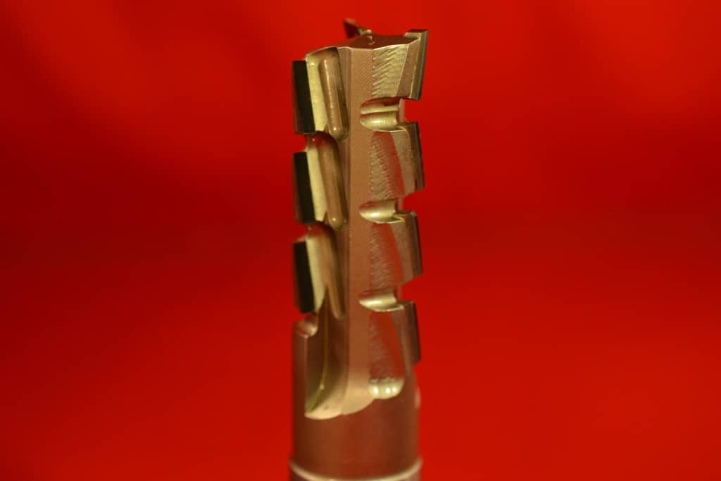 Gold-colored drill bit with serrated edge on red background.