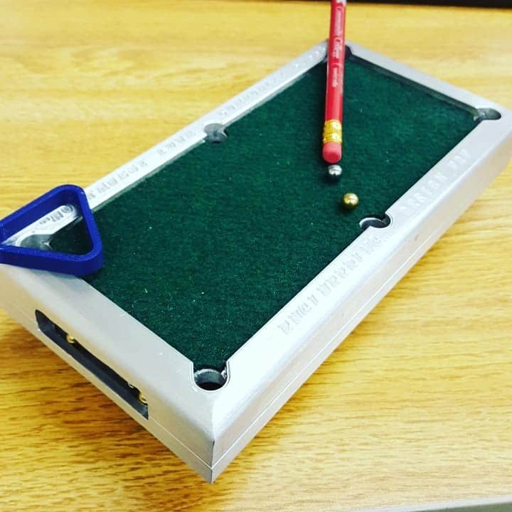 Miniature pool table with green felt, white borders, red cues, and colored balls.