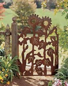 Decorative metal gate with sunflower design in a garden.