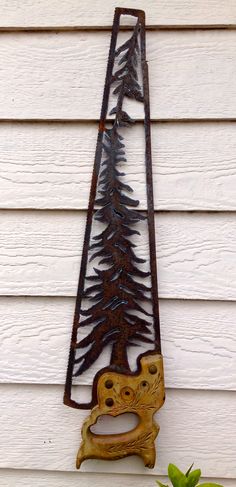 Rusty saw blade with pine tree design hung on a wooden wall.