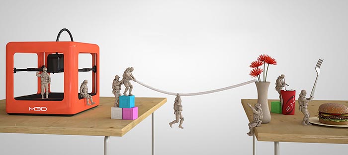 A vibrant orange 3D printer with prominent "M30" logo sits atop a light-colored wooden table with two small military figurines nearby.