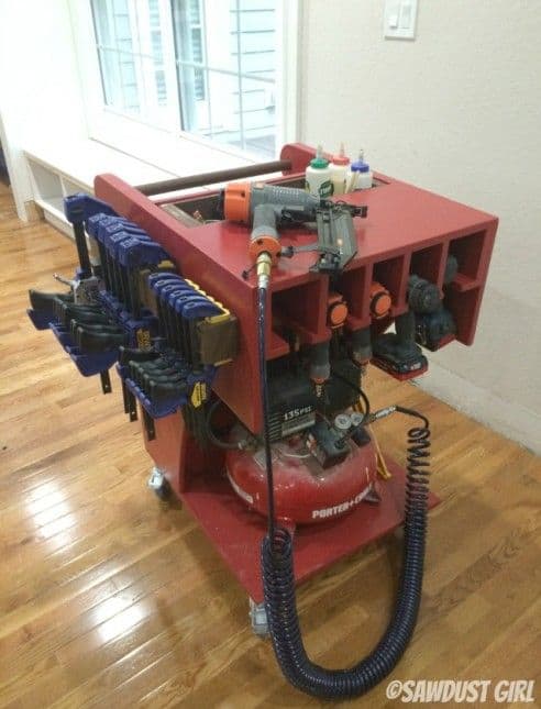Red portable compressor cart with attached tools and black hose on a white background.