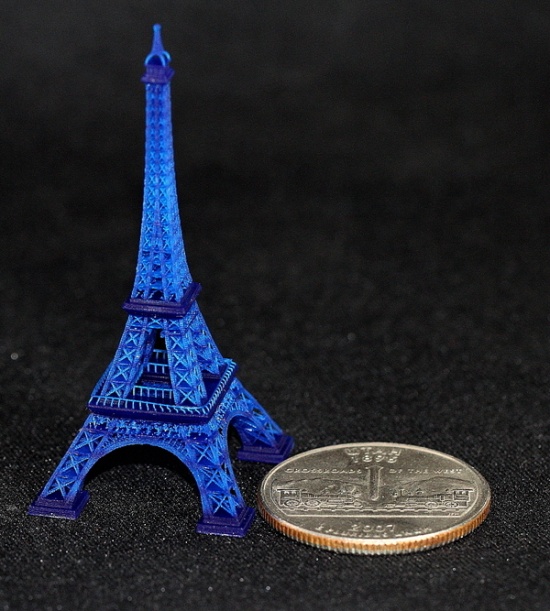 Blue Eiffel Tower model with star pattern, beside a quarter on black background, in miniature scale.