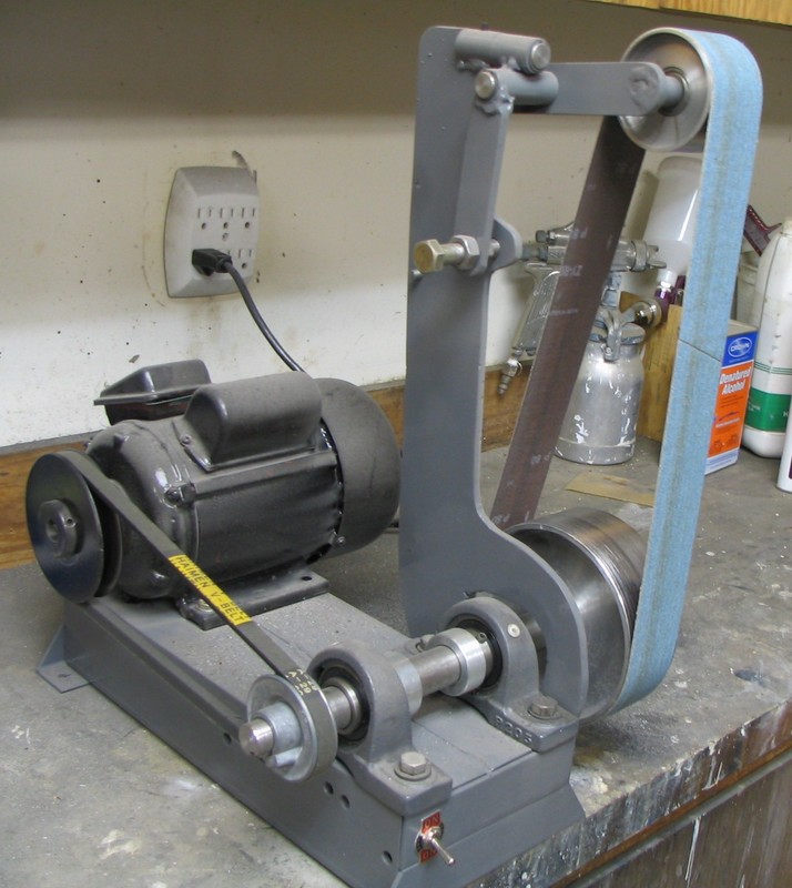 Industrial belt sander on a workbench in a machine shop or workshop.