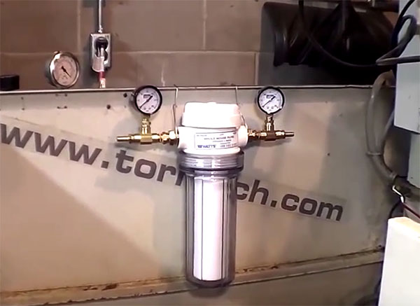 Water filtration system mounted on wall with gauges, valves, and pipes in front of a metal sheet with www.torntech.com logo.