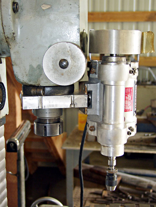 Close-up photograph of a drill press spindle with metal body and central hole for drill bit.