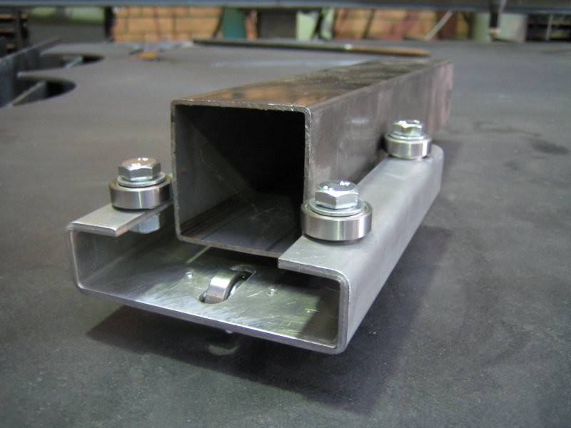 Metal component with two pieces held by four bolts, featuring a hollow top and flat bottom section.