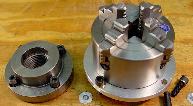 Silver metal 4-jaw chuck adapter plate with 4-inch diameter and central threaded hole.