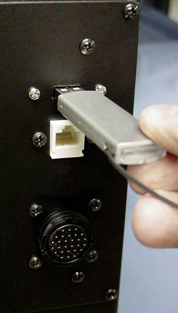 Hand holding USB drive inserted into the back of a black metal device.
