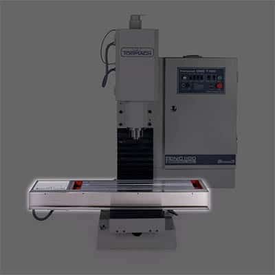 Grey metal milling machine on a flat table with controls.