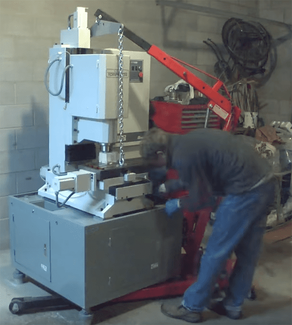 Man lifting large white machine with red crane in industrial setting.