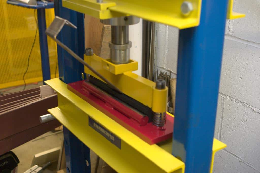 Hydraulic press brake attachment with yellow and blue components on a red base plate.