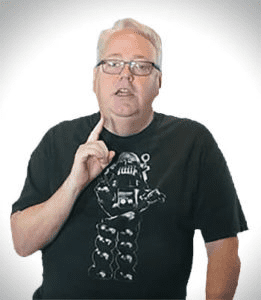 Man with white hair standing in front of a plain background.
