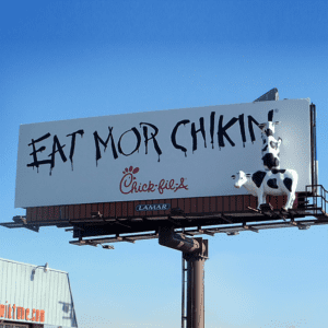 Cow standing in front of Chick-fil-A logo on a blue sky.