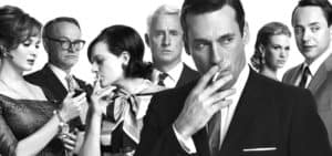 Five formally dressed individuals in 1950s-60s attire, one of whom smokes a cigarette.