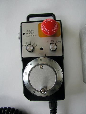 CNC machine control panel with red button and knobs.