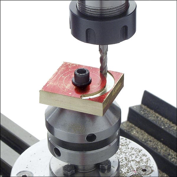 Metalwork machine drilling operation in progress on red metal piece.