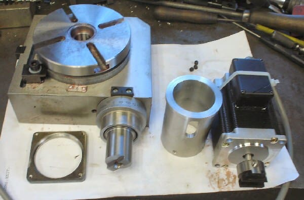 Metal components, including stepper motor table, arranged on a white surface.
