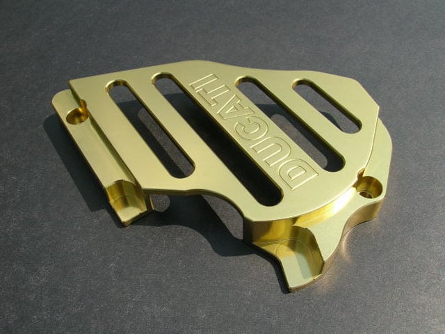 Gold-colored metal part with engraved text: DUCATI.