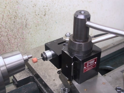 Black metal device with cylindrical body and red label, flat base plate and extension arm, with small orange knob.