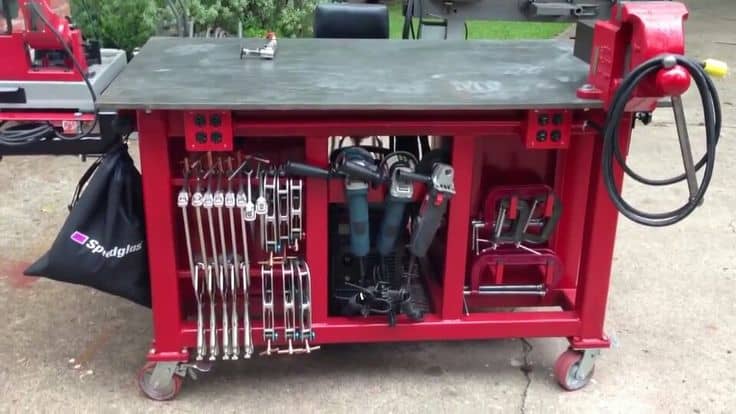 A red metal table on wheels with a grey top, black bag, and various tools and machinery parts.