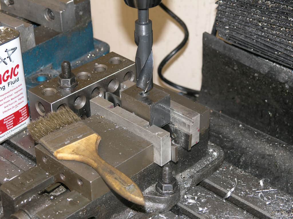 A drill press with a drill bit, surrounded by metal shavings and workshop tools.