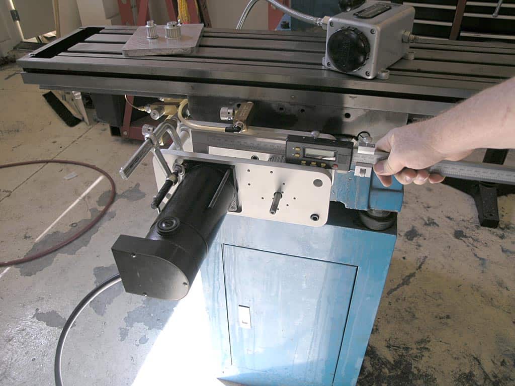 A person's hand holding a metal rod on the front of an industrial machine in a workshop.