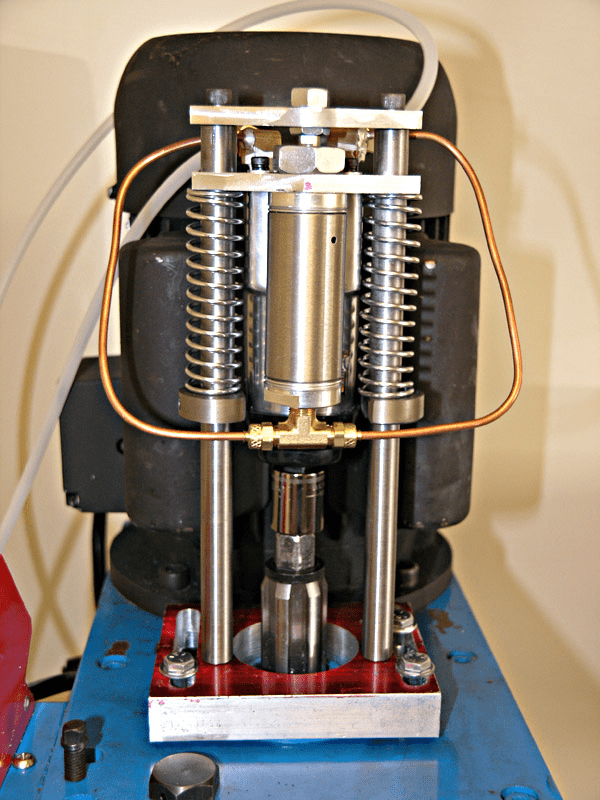 Large metal machinery with springs and copper tubes, mounted on a blue base.
