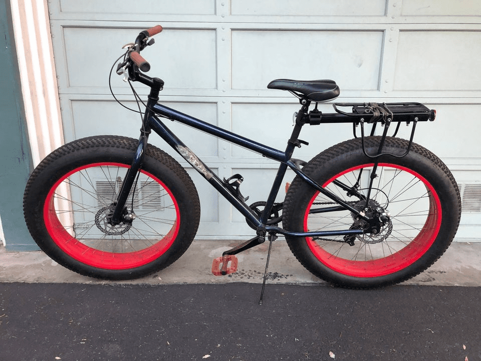 Black fat-tire bicycle with red rims parked in front of white garage door.