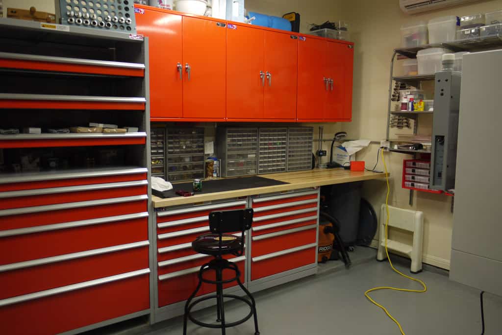 A well-organized garage or workshop with hand tools, power tools, measuring devices, safety gear, workbench, and shelving unit containing various materials.