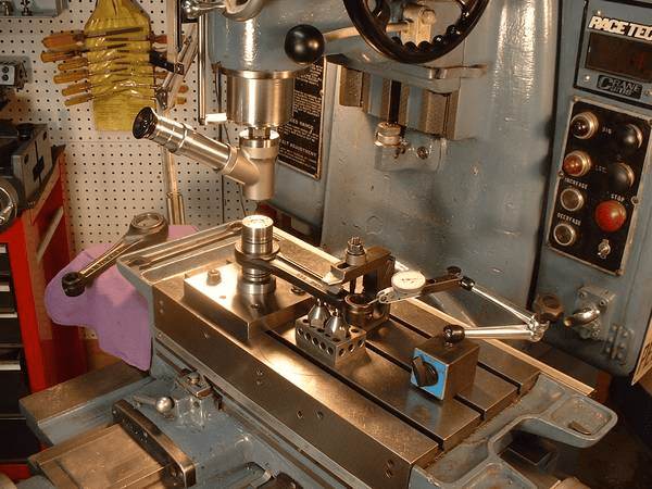 A large metal machine with tools attached, having a flat surface and a long arm with a drill bit.